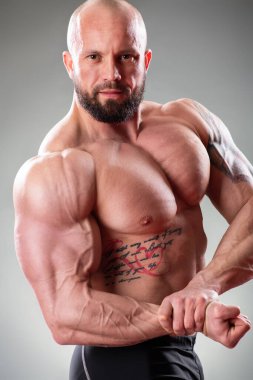 Gri arka planda poz veren seksi kaslı vücut bulucuyu kapat. Biceps kasılması