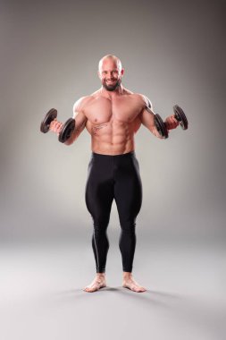 Gri arka planda ağırlıkları olan seksi kaslı vücut bulucu
