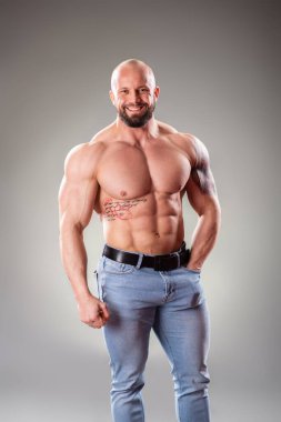 Gri arka planda seksi kaslı vücut bulucu pozu