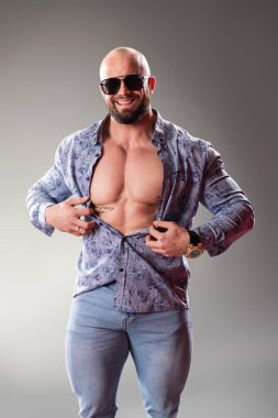 Sexy unbuttoned muscular bodybuider with sunglasses on the gray background clipart