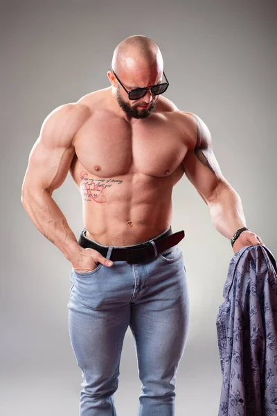 穿着灰色背景太阳镜的性感肌肉健美者扔掉了他的衬衫 — 图库照片