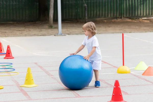 Güzel Küçük Çocuk Spor Poligonunda Büyük Mavi Topu Yuvarlıyor — Stok fotoğraf