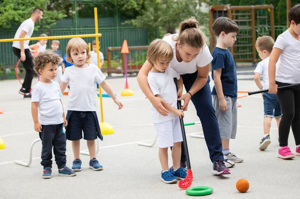 Bir grup çocuk çokgen içinde hokey oynuyor. Spor okulu. Koç yardım ediyor