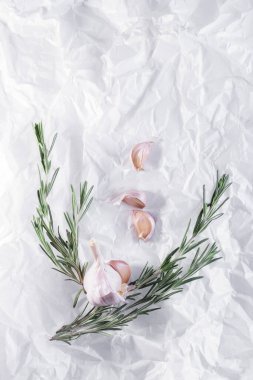 Beyaz parşömen kağıdında bir baş sarımsak (az karanfil) ve biberiye.