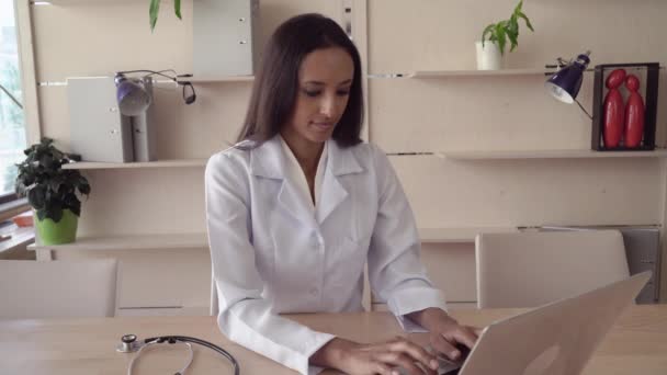 Beautiful nurse sits at the wooden desk with laptop. — Stock Video