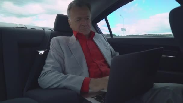 Мужчина средних лет, использующий ноутбук в машине, сидит на заднем сидении . — стоковое видео