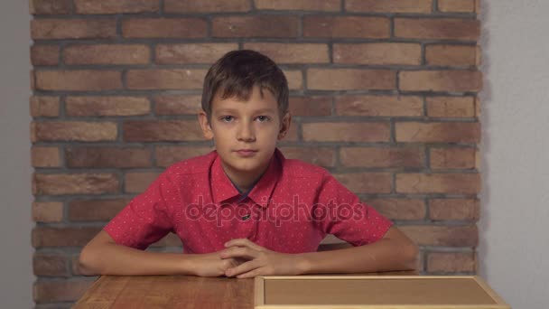 Niño sentado en el escritorio sosteniendo el rotafolio con el jefe de letras en la pared de ladrillo rojo de fondo . — Vídeos de Stock