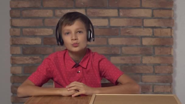 Niño sentado en el escritorio sosteniendo el rotafolio con música de letras en la pared de ladrillo rojo de fondo . — Vídeos de Stock