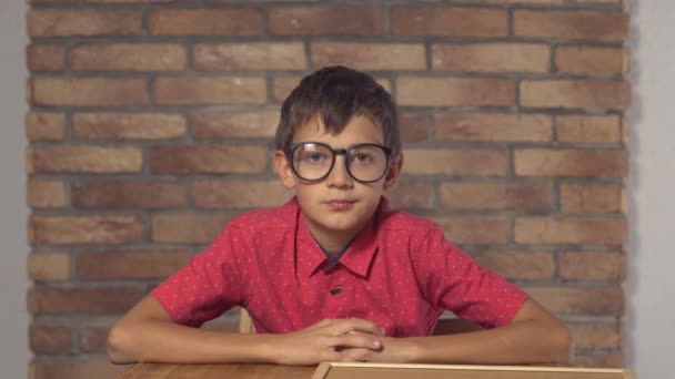 Niño sentado en el escritorio sosteniendo el rotafolio con letras pr en la pared de ladrillo rojo de fondo — Vídeos de Stock