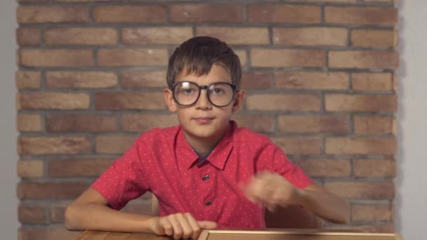 Niño sentado en el escritorio con rotafolio con descuento en letras en la pared de ladrillo rojo de fondo . — Vídeo de stock