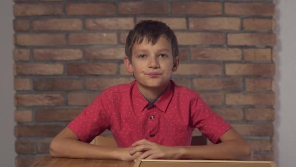 Bambino seduto alla scrivania tenendo flipchart con lettering taxi sullo sfondo muro di mattoni rossi — Video Stock