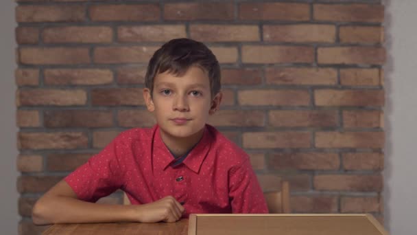 Enfant assis au bureau tenant tableau à feuilles avec tendance de lettrage sur le mur de brique rouge de fond — Video