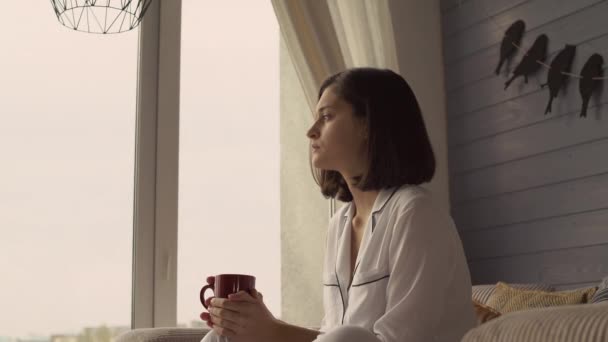 Привлекательная девушка смотрит в окно на уютную квартиру . — стоковое видео