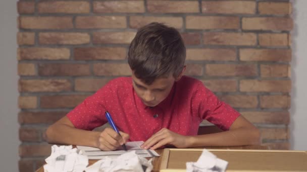 Enfant assis au bureau tenant un tableau à feuilles avec une erreur de lettrage sur le mur de brique rouge de fond . — Video