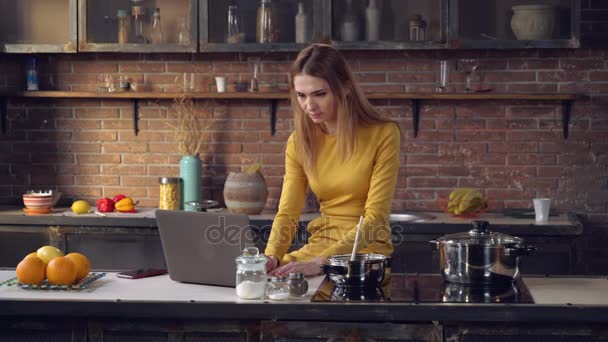 Young lady using computer and cooking lunch. — Stock Video