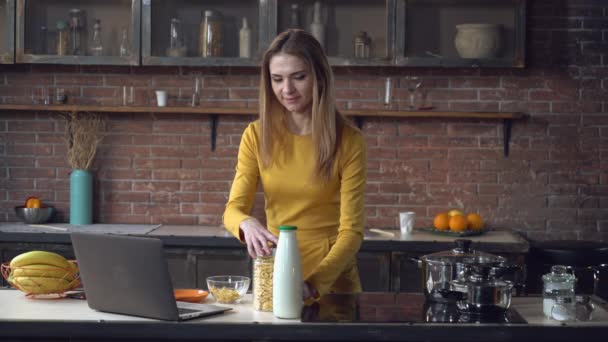 Mujer preparando el desayuno con ordenador en el apartamento . — Vídeo de stock