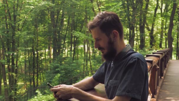 Un hombre guapo con un teléfono inteligente está mirando a la cámara y sonriendo . — Vídeos de Stock