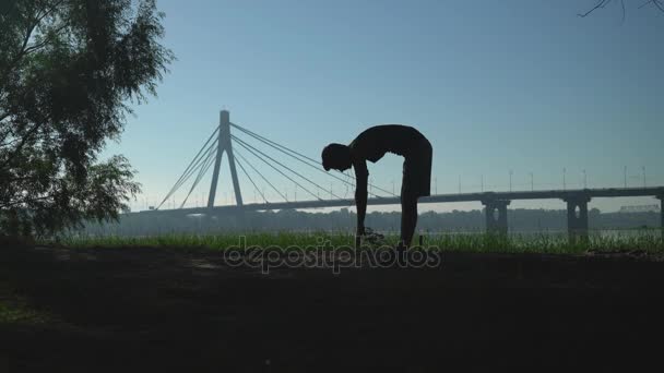 A young man bends down to stretch his back and legs. — Stock Video