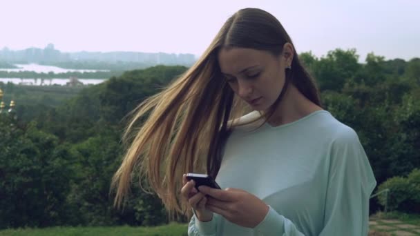Женщина смотрит на телефон с волосами, играющими с ветром. . — стоковое видео