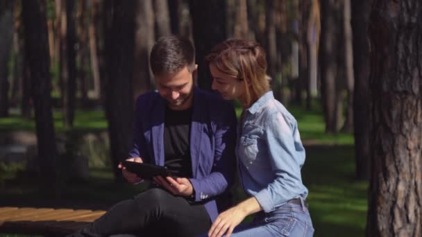 Pareja usando dispositivo moderno y riendo al aire libre . — Vídeos de Stock