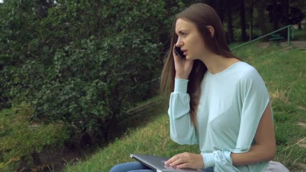 Güzel bir kız parkta oturan ve telefon üzerinde konuşuyor. — Stok video