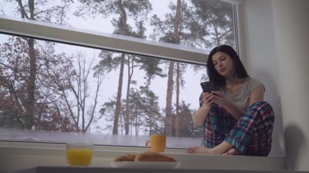 Feminino segurando móvel sentar no peitoril da janela — Vídeo de Stock