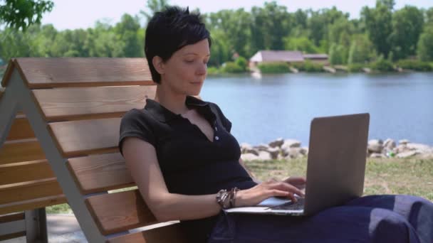 Chica charlando en pc sentado cerca del río . — Vídeos de Stock