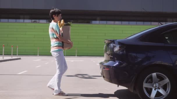 Mujer va con productos alimenticios en el aparcamiento . — Vídeos de Stock