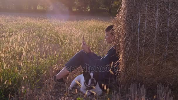 在草甸与法国斗牛犬拿着智能手机的女孩. — 图库视频影像