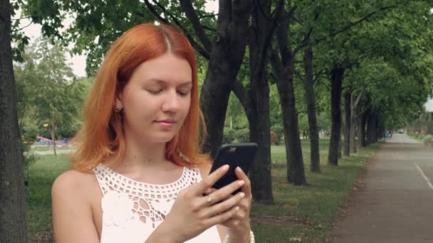 Estudiante de jengibre utilizando el teléfono inteligente al aire libre . — Vídeos de Stock