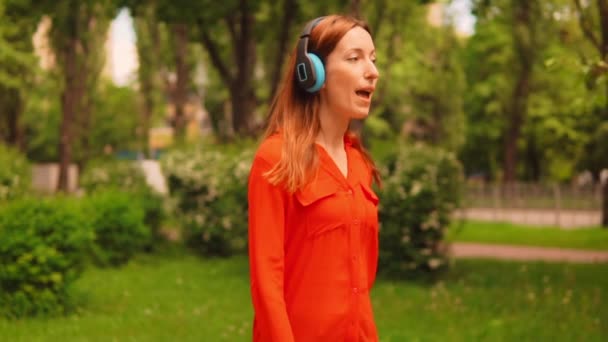 Side view caucasian female in red shirt going and dance along the alley — ストック動画