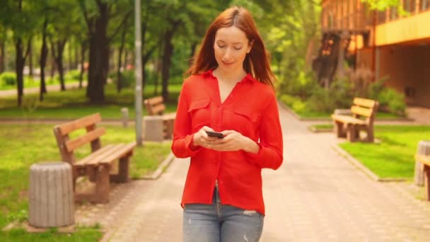 Μια κοκκινομάλλα επιχειρηματίας που κρατά κινητό περπάτημα — Αρχείο Βίντεο