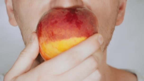 Close up gezicht eerlijk man eet rood perzik — Stockvideo