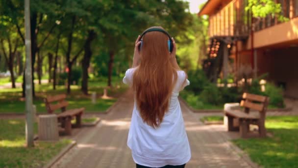 Невизначена жінка в навушниках прогулянка в парку — стокове відео