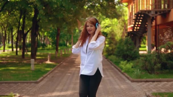 Pelirroja femenina en auriculares pasear por el parque — Vídeos de Stock