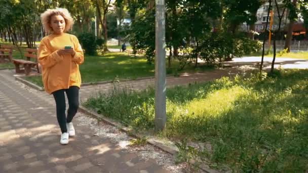 Student in bright sweater typing message on the run — Stock Video