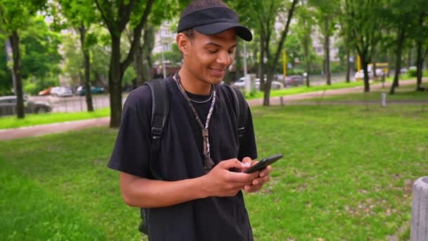 Lächelnder Typ tippt Nachricht auf Handy im Freien — Stockvideo