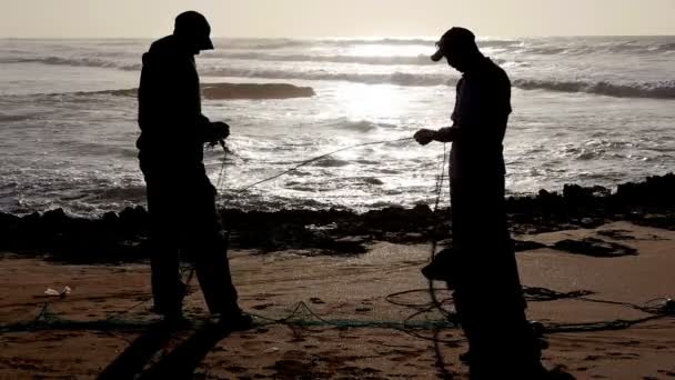 Twee vissers in silhouet repareren een Oceaan vissen net in Marokko Slow motion — Stockvideo