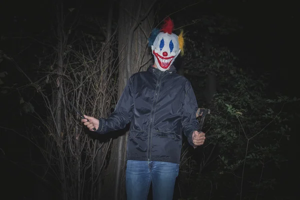 Страшний клоун в дереві з ножем і сокирою — стокове фото