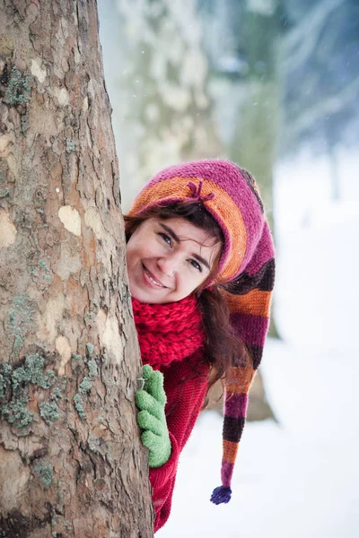 Усміхнена молода жінка в сніжному парку за деревом — стокове фото