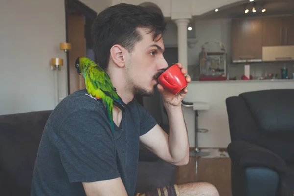 Young man with his pet parrot drinking coffee — Stock Photo, Image