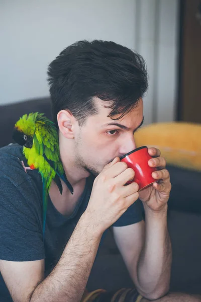 Young man with his pet parrot drinking coffee — Stock Photo, Image