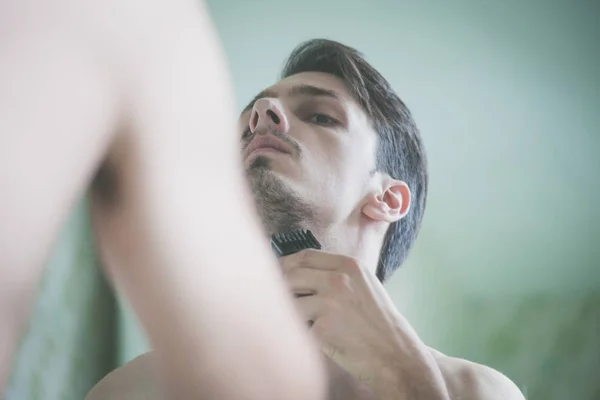 Close-up van jonge man trim baard voor spiegel — Stockfoto