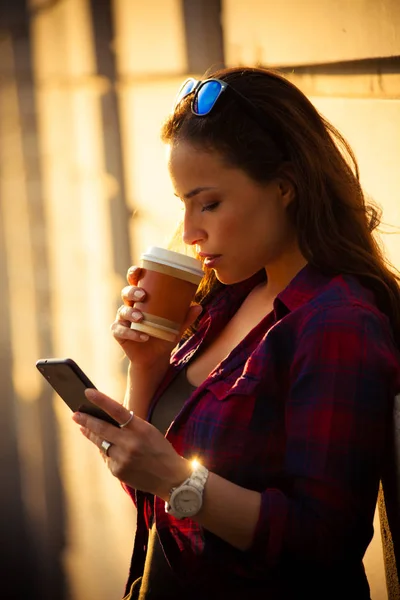 Девушка в городе со смартфоном и кофе на вынос — стоковое фото