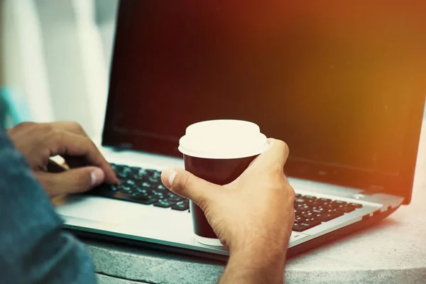 Man hands using laptop and holding cup of coffee outdoor closeup — Stock Photo, Image