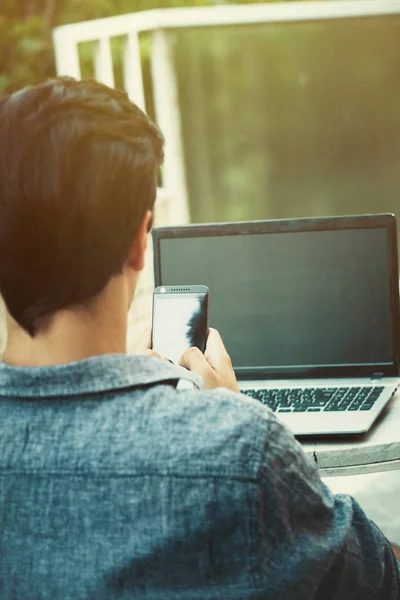 Young man working from terrace with smartphone and laptop — Stock Photo, Image