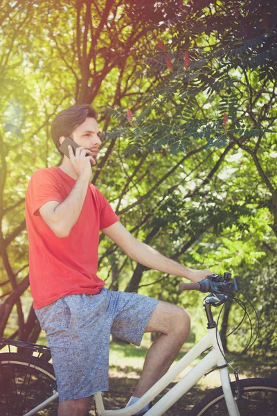 young man on bike in wood with smartphone