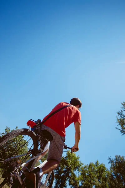 Joven montar en bicicleta desde abajo tiro de espalda — Foto de Stock