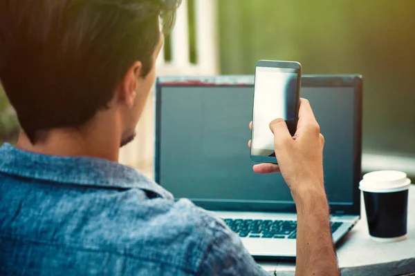 Hombre joven al aire libre en la terraza con ordenador portátil y teléfono inteligente de trabajo —  Fotos de Stock