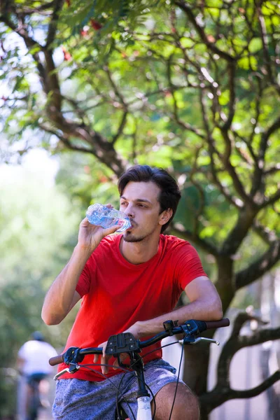 Joven hombre sentarse en bicicleta en madera descansando beber agua — Foto de Stock